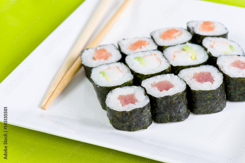 Tuna and salmon sushi rolls with chopsticks on a white plate on a green mat Tuna and salmon sushi rolls with chopsticks on a white plate on a green mat
