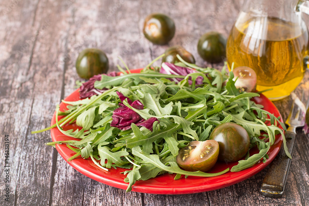 Green salad. Fresh green salad with tomatoes on a red plate, next to a glass jug with olive oil.
Green salad. Fresh green salad with tomatoes on a red plate, next to a glass jug with olive oil.