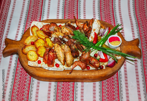 Assorted barbeсue plate. Grilled potato and meat platter- beef, pork ribs, quails, chicken fillet served with flatbread, chili pepper, red onion, dill, horseradish and mustard on a large wooden tray.