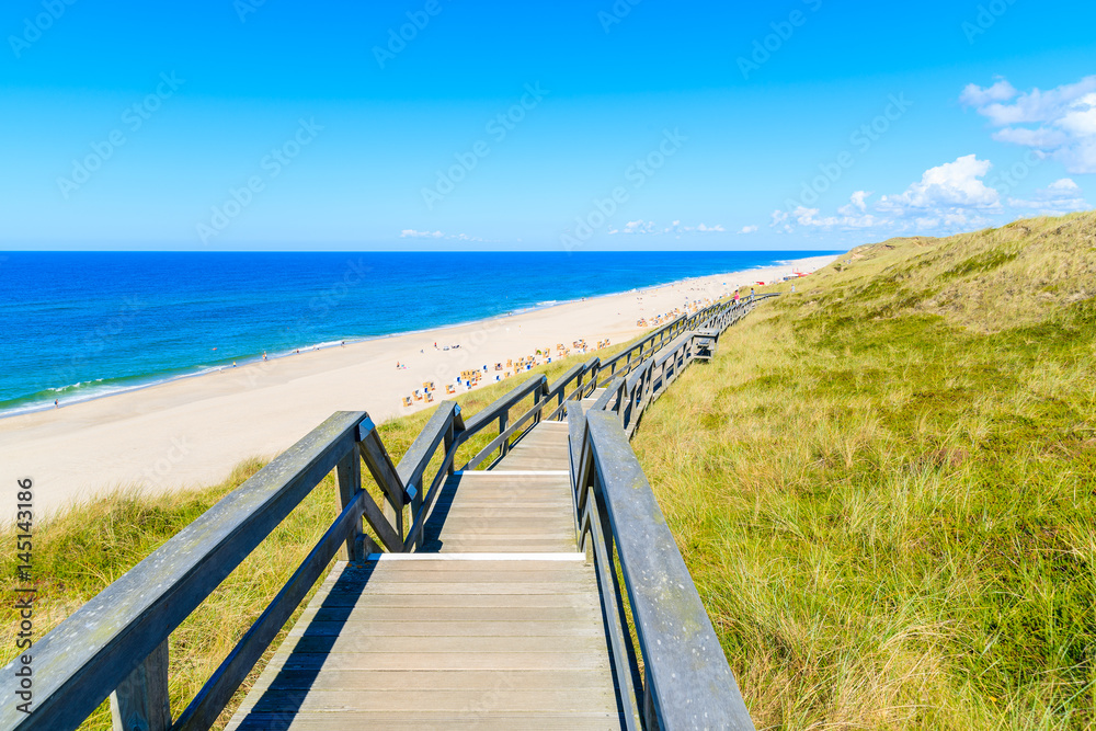 Obraz premium Wooden walkway along a coast of North Sea and view of beautiful beach near Wenningstedt village, Sylt island, Germany