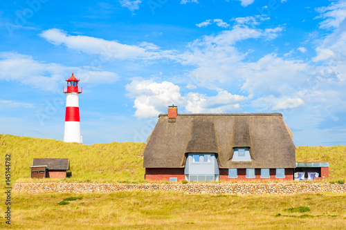 Ellenbogen lighthouse and house with straw rof on sand dune against blue sky with white clouds on northern coast of Sylt island, Germany photo