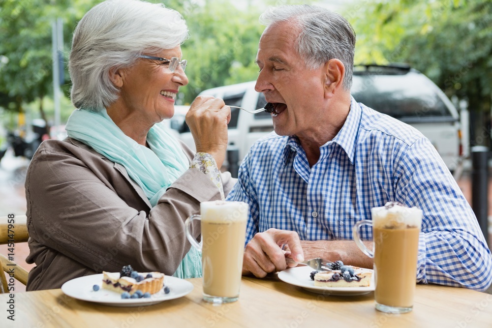 Senior woman feeding tart to man in café Senior woman feeding tart to man in café