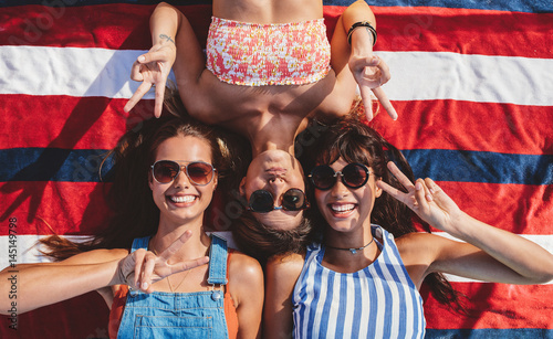 Smiling female friends with peace sign lying at the beach photo