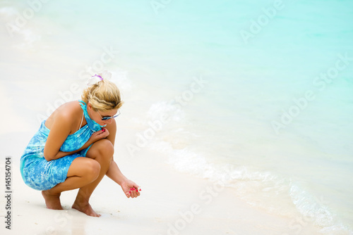 Woman crouching and touching little shells on the white sand beach.Copy space