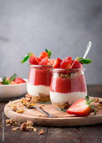 Delicious homemade granola, yogurt and strawberry parfait in glass jars on rustic wooden background