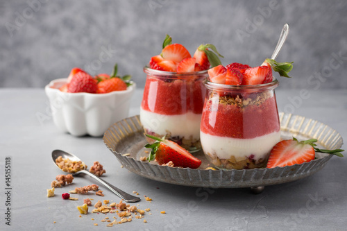 Delicious homemade granola, yogurt and strawberry parfait in glass jars on concrete background