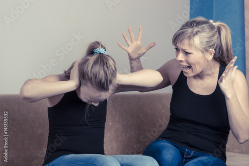 Fotografija Beautiful young mother is scolding her daughter while sitting on sofa at home