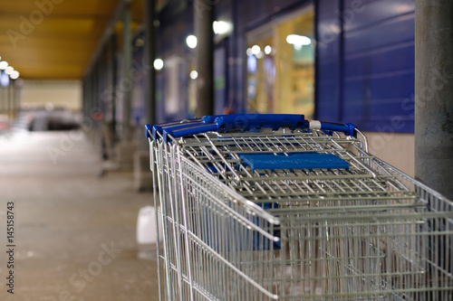 Row of stacked shopping carts with blue handles near exit of supermarket in night