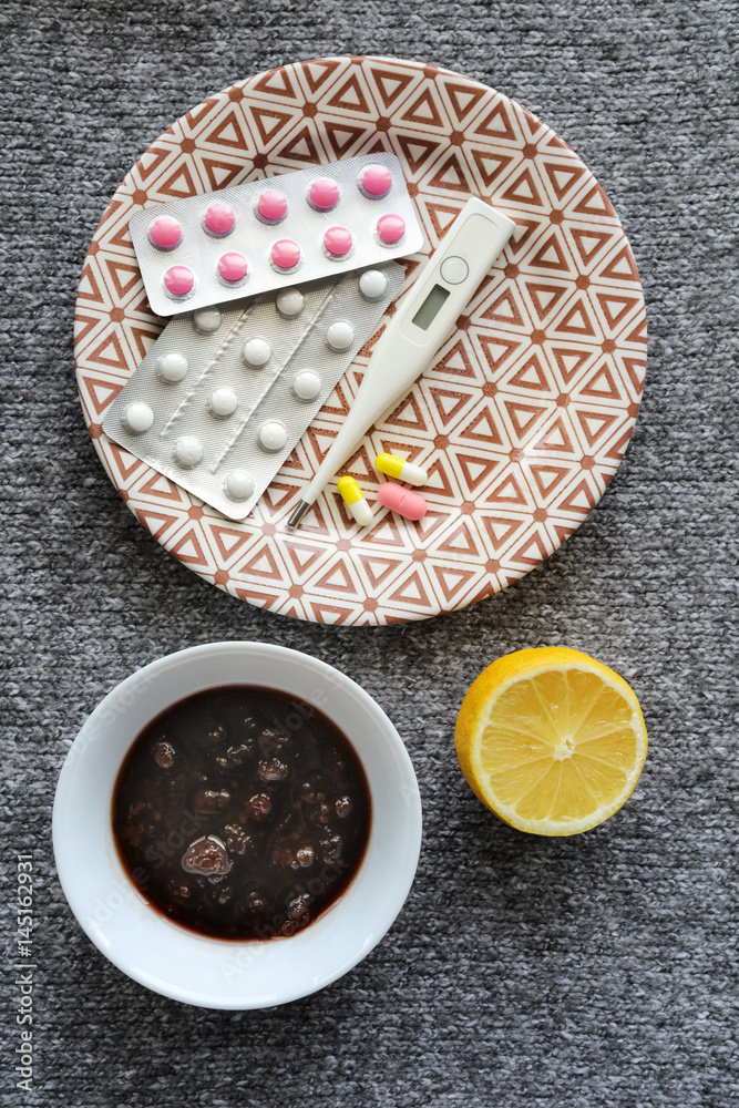 Thermometer, jam, lemon, tablets for colds on the grey background Thermometer, jam, lemon, tablets for colds on the grey background