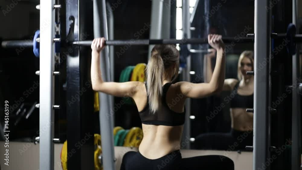 Young attractive girl in gym doing exercise in smith machine 