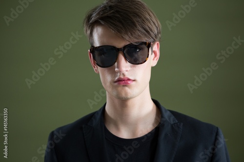 Androgynous man in sunglasses posing against green background © wavebreak3
