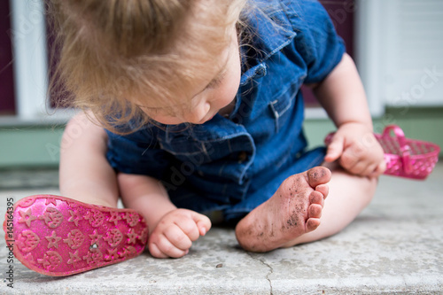 Young girl with one shoe off inspecting dirty foot
