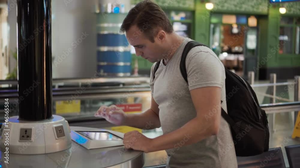 Handsome young man in airport terminal. Standing near charging stand pluging in smartphone