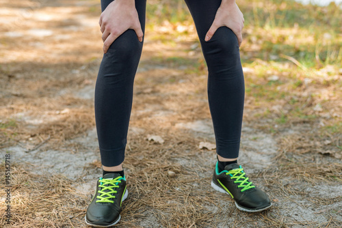 Girl in sports pants and hoodie, standing holding on to her knees. Rest after running