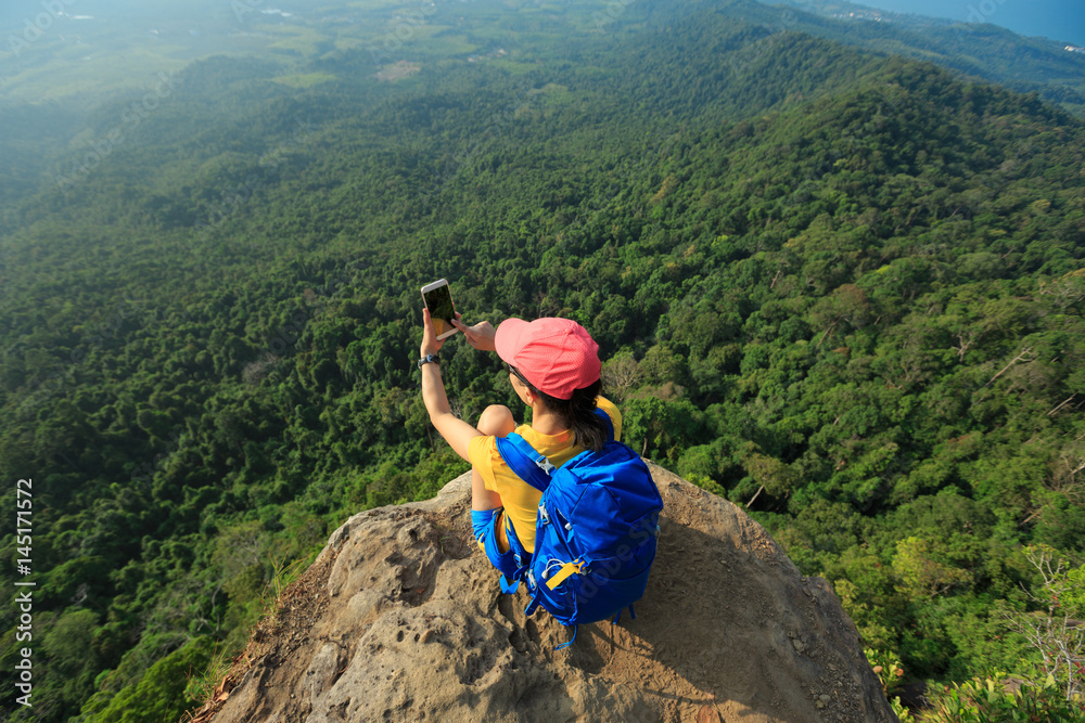 successful woman hiker taking photo with cellphone hiking on mountain peak