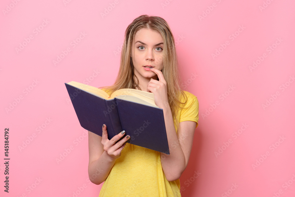 Confused cute girl thinking and reading the book isolated on colorful pink background Confused cute girl thinking and reading the book isolated on colorful pink background
