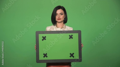 Young female with negative expression on face holding chromakey board and looking at camera. Chromakey with cross for tracking good for inserting some pictures or 3d graphic or commercial inscription photo