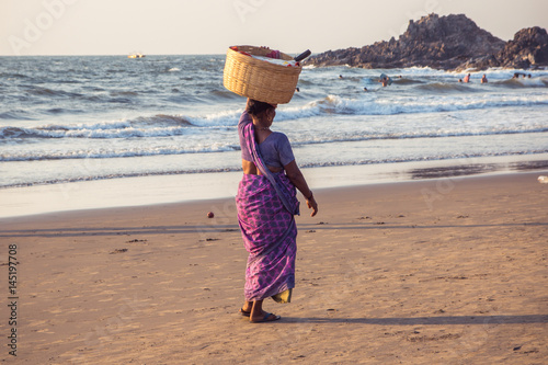 GOA, INDIA - MARCH 4: Woman in saris with basket on her head walks by Vagator beach on March 4, 2017 in Goa, India