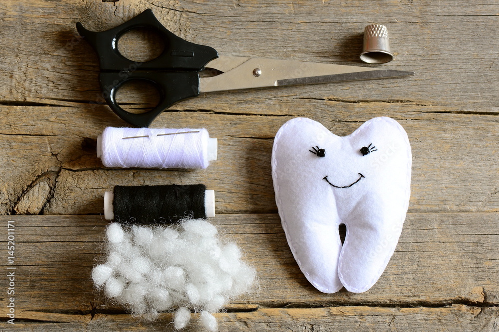 Fototapeta premium Making a felt tooth fairy. Step. Tutorial. Stuffed felt tooth fairy toy, scissors, thread, thimble, needle, filler on vintage wooden table. Simple and fun sewing crafts for kids. Top view. Closeup