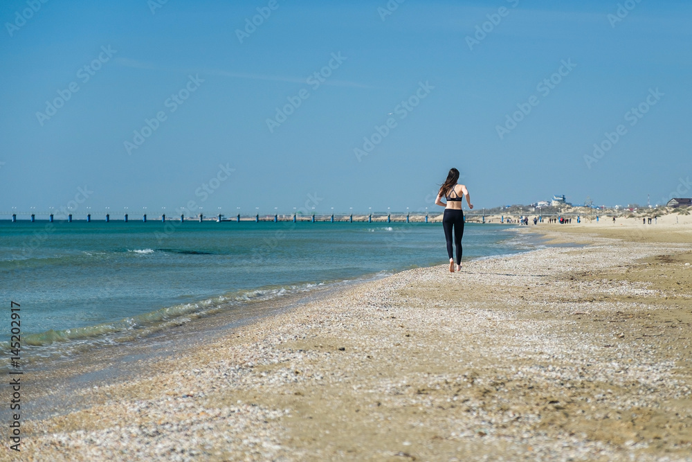 Beautiful young woman Jogging on the beach, rear view