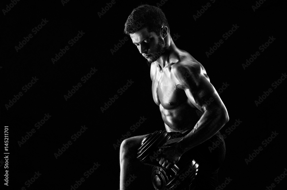 Young determined sportsman working out shirtless showing off his strong muscular body lifting weights copyspace monochrome shot dumbbells equipment gym fitness sport motivation biceps concept.