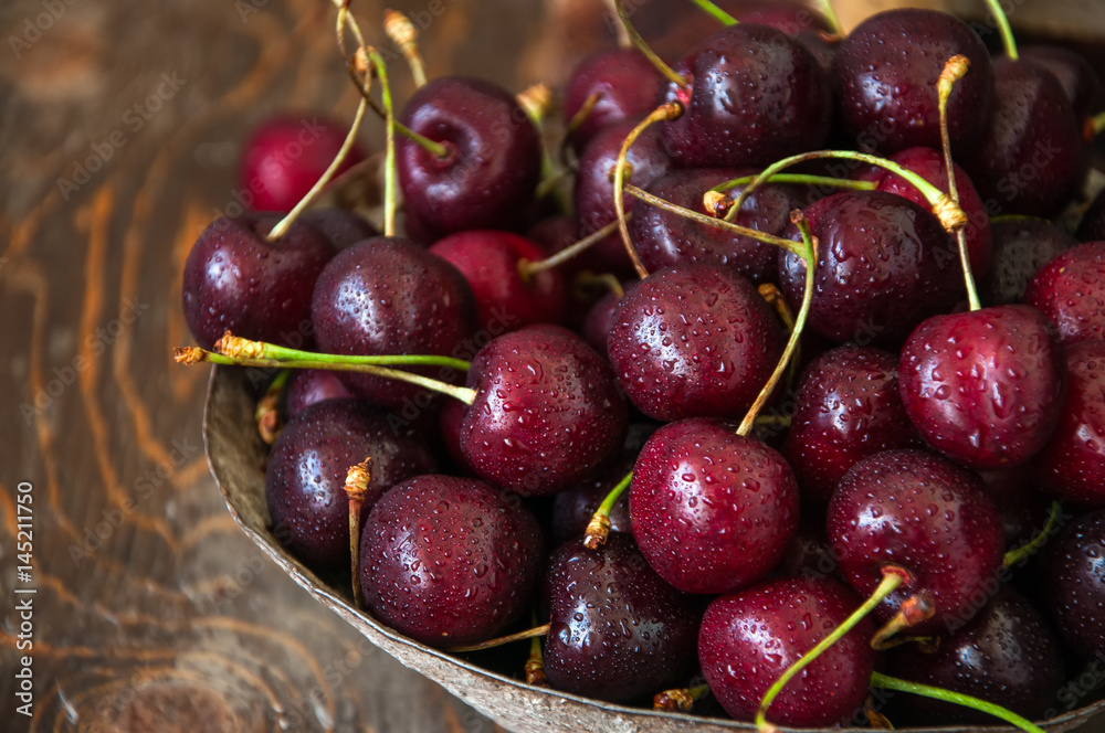 Sweet fresh ripe burgundy cherries with water drops in a bowl on a wooden background. Close up and copy space. Sweet fresh ripe burgundy cherries with water drops in a bowl on a wooden background. Close up and copy space.