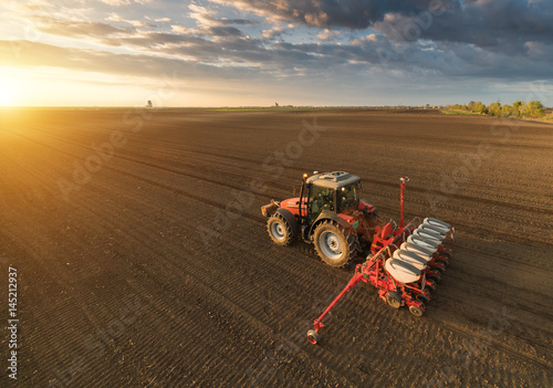 Farmer with tractor seeding - sowing crops at agricultural field in spring
