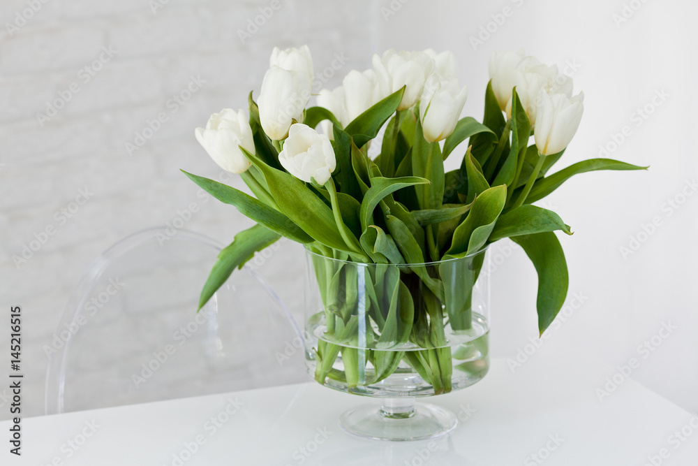 Naklejka premium Białe tulipany w szklanym przeźroczystym wazonie na białym tle.