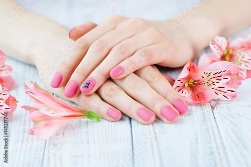 Woman hands with pink matted manicure on finger nails and delicate flowers