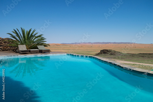 Pool with Palm and Sun Beds in a Desert Landscape near Solitaire, Namibia © MilesAstray