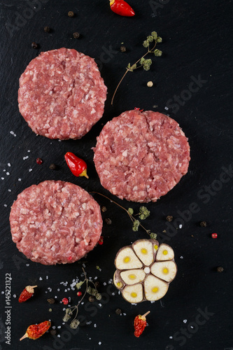 Fresh raw meat burger cutlet on the black slate board with herbs and spices for background. top view ..