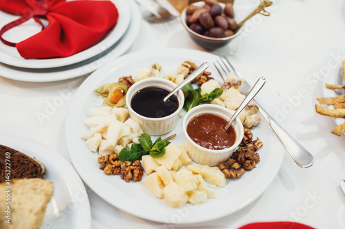 Bowls with sauces stand on plate with nuts and cheese