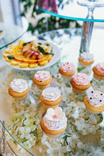 Little cakes with white cream and berries on glass table