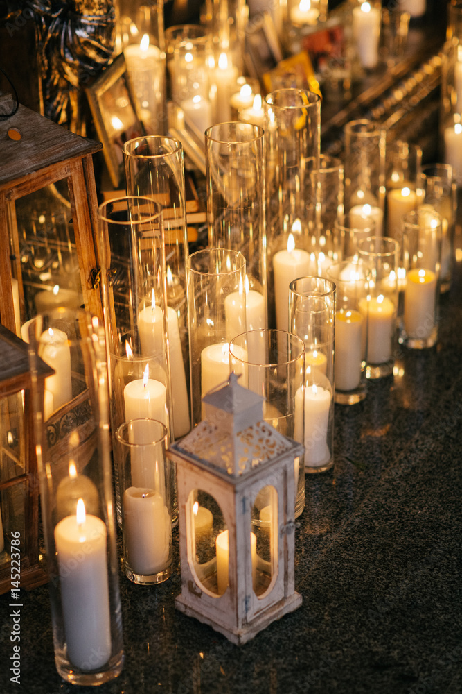 Shiny candles in tall glass vases stand on marble floor Photos | Adobe Stock