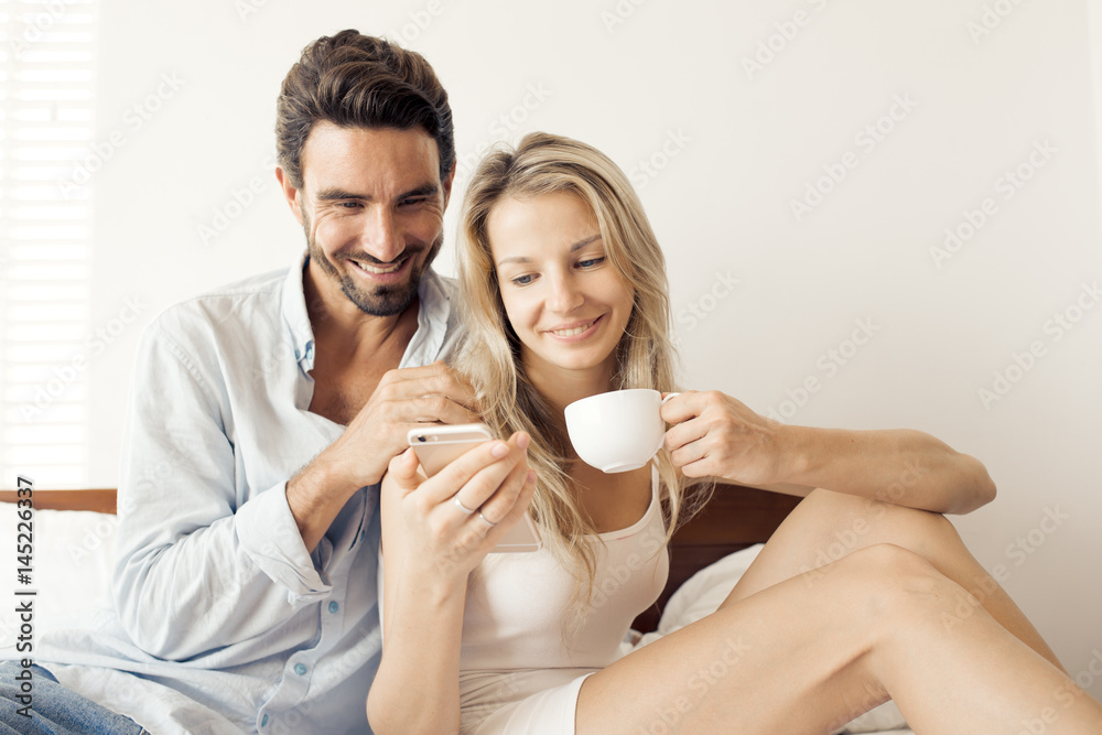 Happy attractive smiling couple sitting on bed in bedroom Happy attractive smiling couple sitting on bed in bedroom