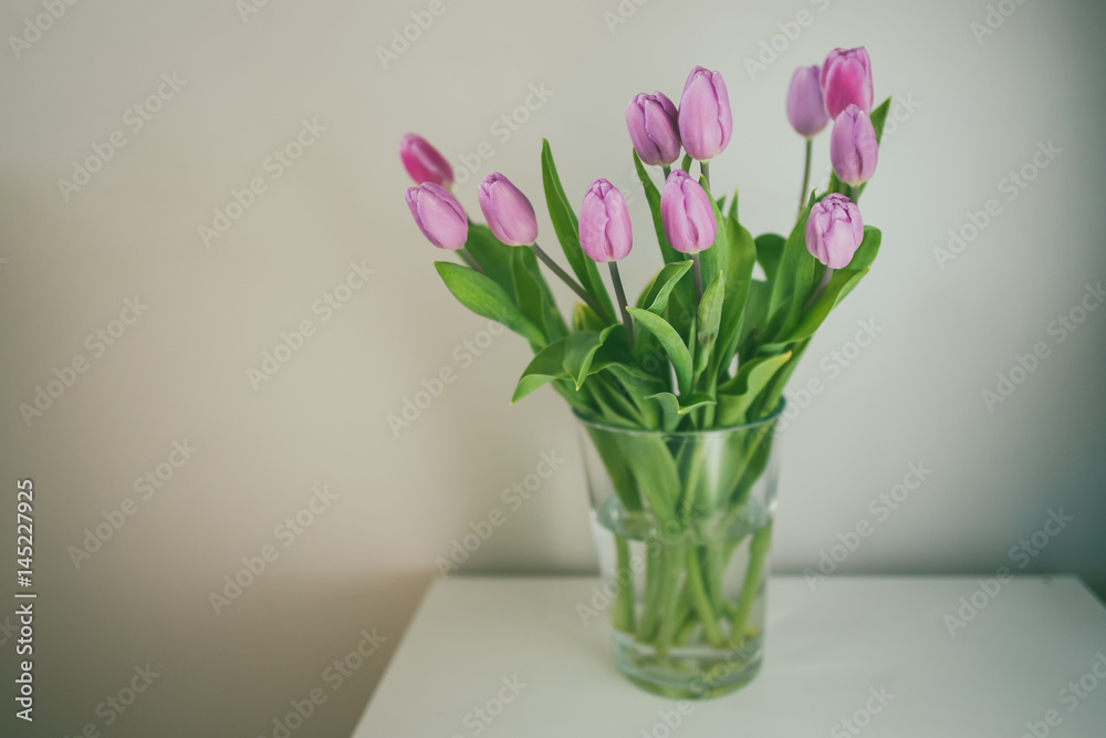 Fototapeta premium Fresh pink tulip flowers bouquet in a glass jar on white table