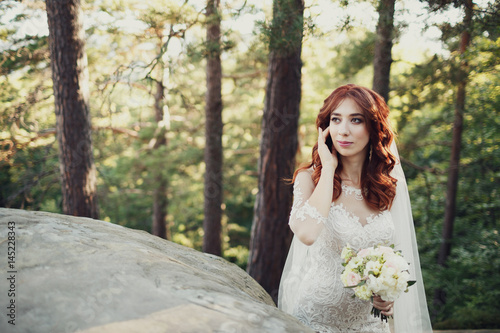 Bride with red hair looks stunning standing on the rocks in the park