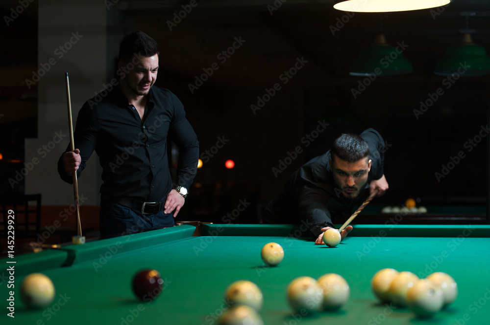 Fototapeta premium Two male friends playing billiard game in club