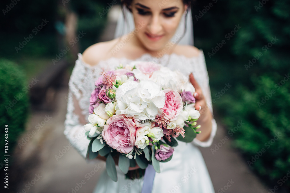 Naklejka premium The beautiful bride keeps a bouquet and walking along park