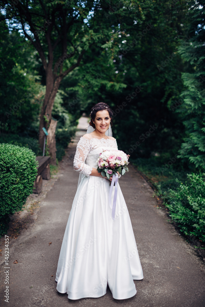 The beautiful bride keeps a bouquet in the park