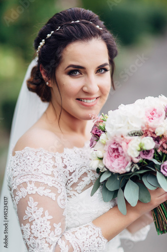 The beautiful bride keeps a bouquet in the park