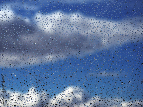 Water drops at the window glass at the blue sky with the rainy clouds background
