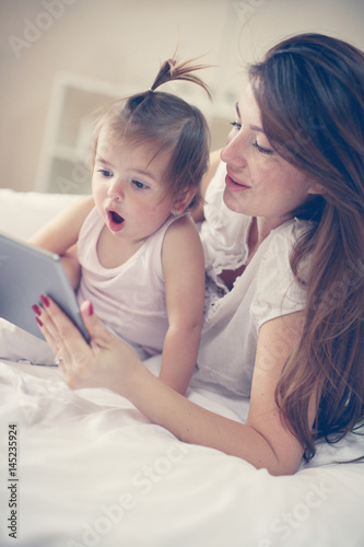 Mother and her little baby at home. Mother with her baby using tablet in the bed.