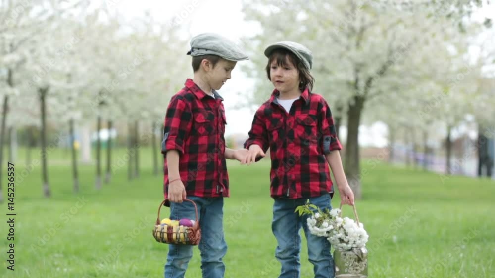 Two children, boy brothers, having fun with easter eggs in the park, beautiful spring blooming garden