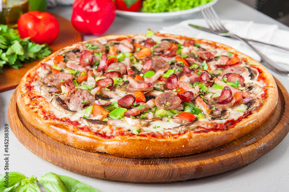 Selective focus close up Delicious Meat Pizza with bacon and sausages on the wooden board on the kitchen table with different bright ingredients Selective focus close up Delicious Meat Pizza with bacon and sausages on the wooden board on the kitchen table with different bright ingredients