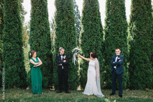 Funny wedding couple and friends pose before green trees in park