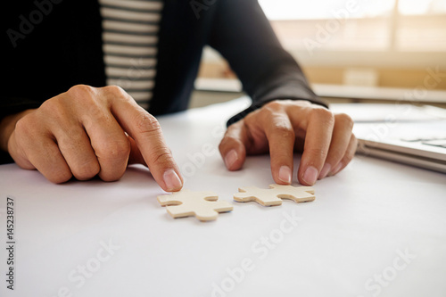 Asian business woman hands on a wooden office desk pick puzzle. Business solutions success and strategy concept. Businessman hand connecting jigsaw puzzle.Close up photo with selective focus.
