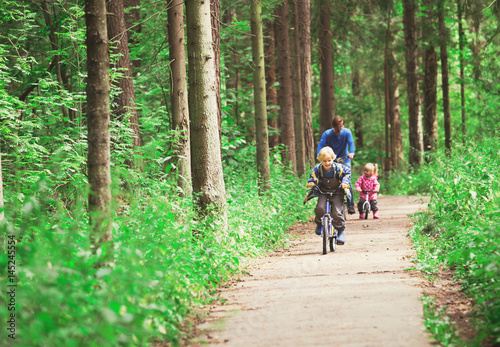 father with two kids riding bikes in nature