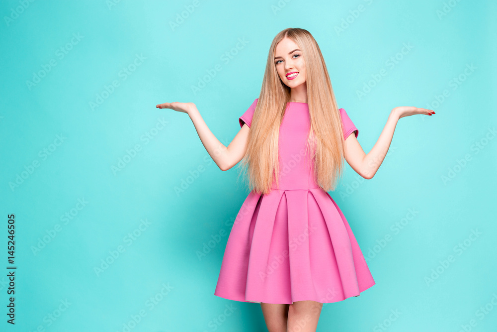 Fototapeta premium Smiling beautiful young woman in pink mini dress posing, presenting something