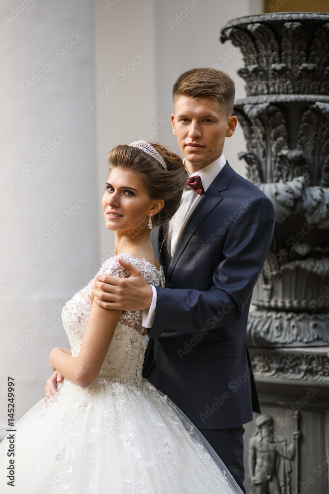 Fototapeta premium Groom holds bride's shoulders standing before tall black vase
